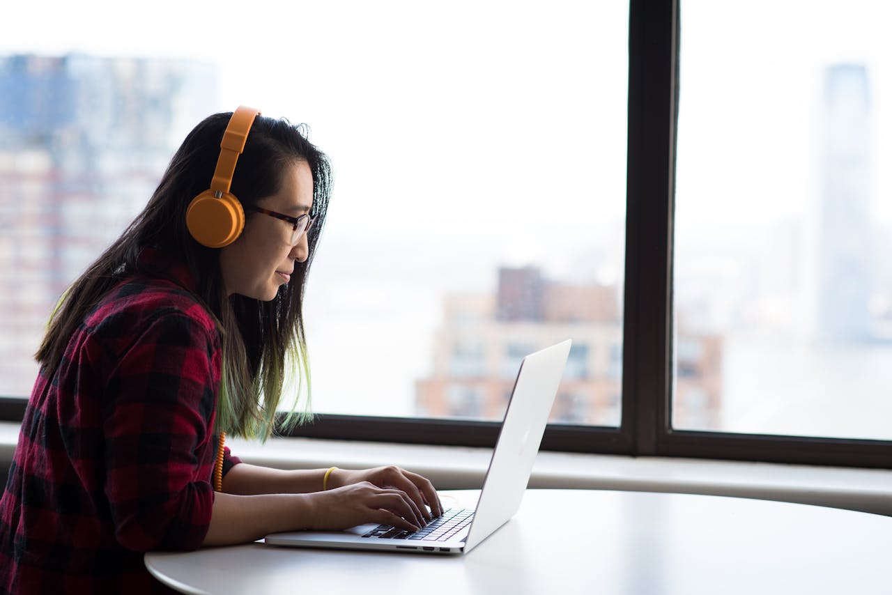 about-01 Asian woman with headphones using laptop for remote work in a city setting.