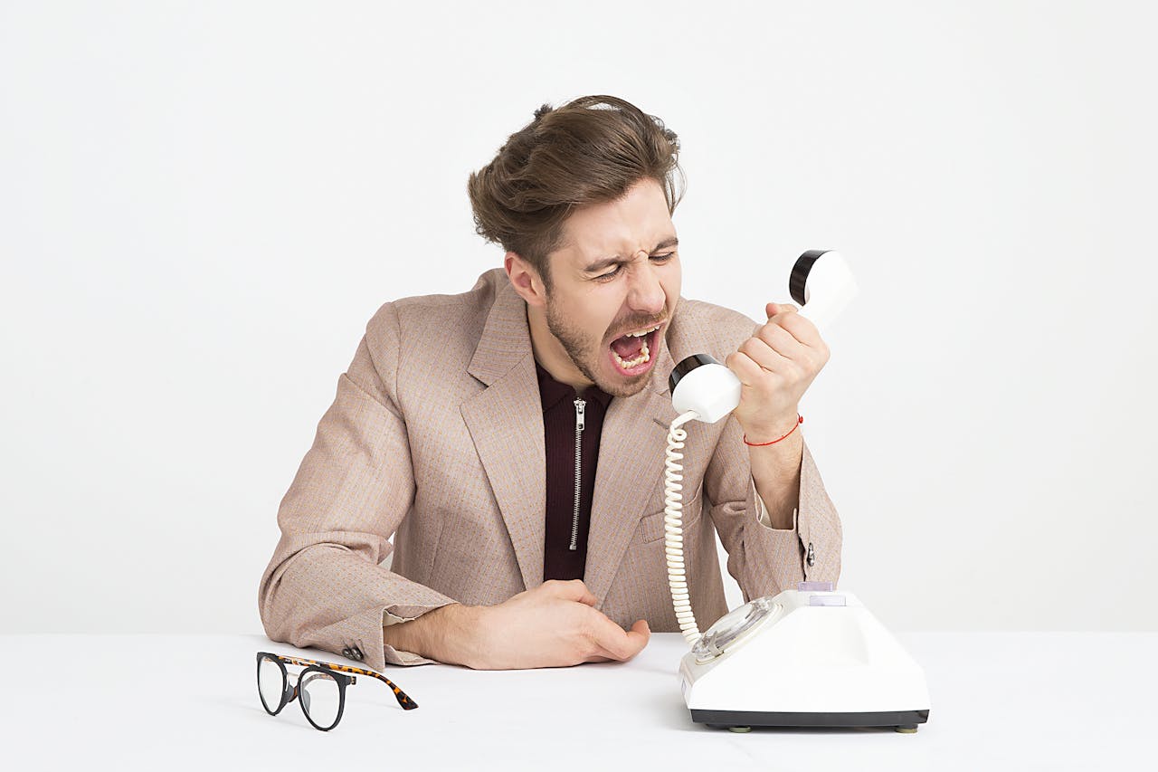 our-services-2 Businessman in a beige suit shouting into a vintage telephone, expressing frustration at work.