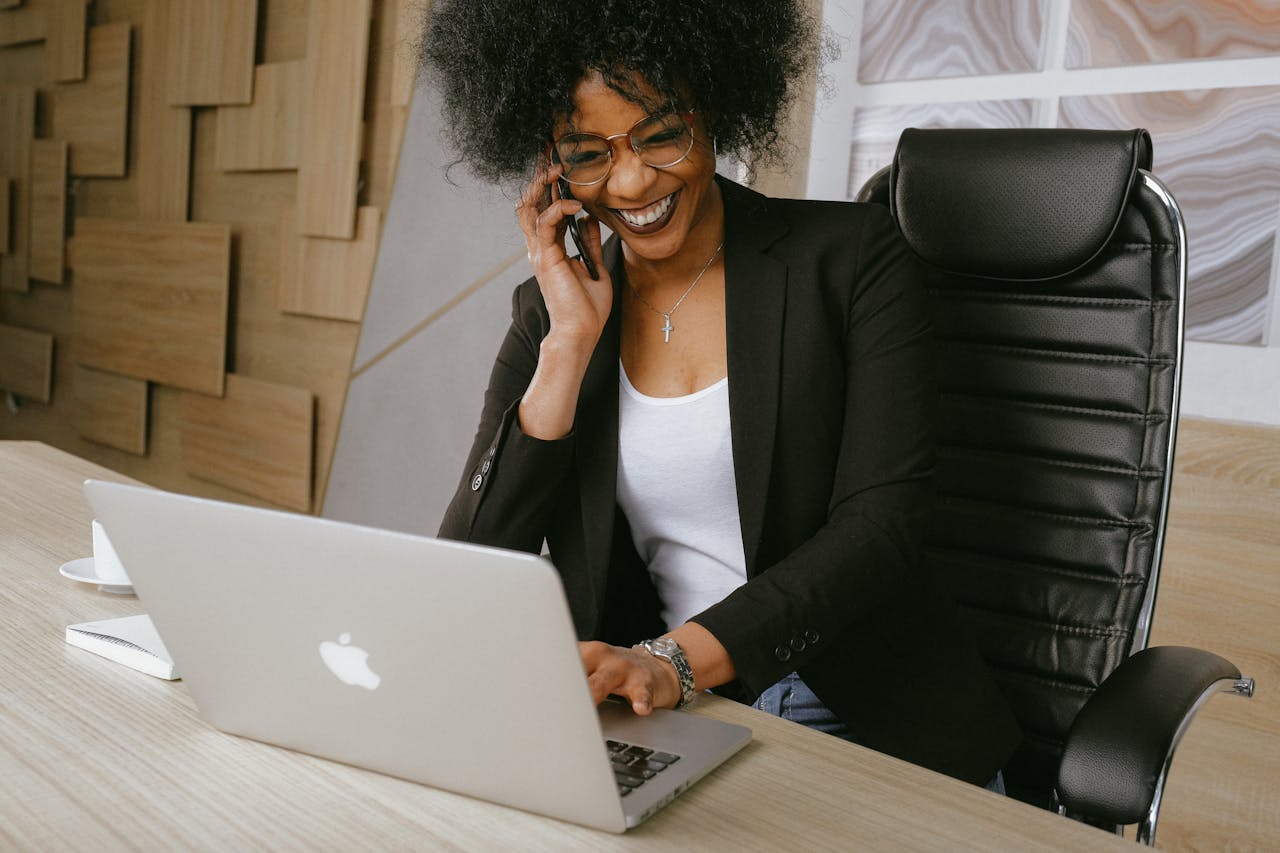 our-services-1 Smiling woman on phone call while working on a laptop in a stylish office.