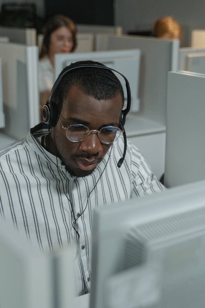 why-choose-us Customer support representative wearing glasses and headset in a busy call center setting.