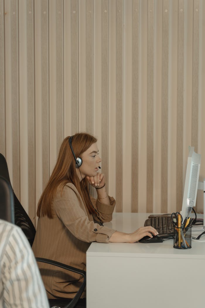 gallery-5 Red-haired woman with headset working at computer desk in office setting.